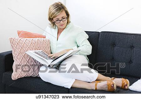 Stock Image - Woman reading book on sofa. Fotosearch