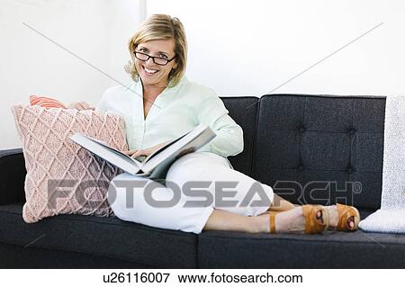 Stock Photo - Woman sitting with book on sofa. Fotosearch