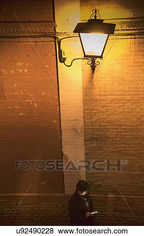 Stock Photo - Woman standing by brick wall and using smart phone. Fotosearch