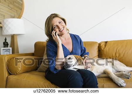 Stock Photography - Woman stroking Labrador Retriever and using mobile phone. Fotosearch