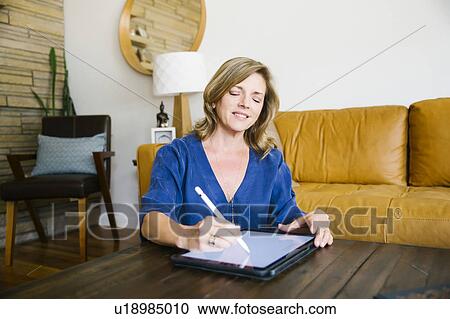 Stock Image - Woman using digital tablet in living room. Fotosearch
