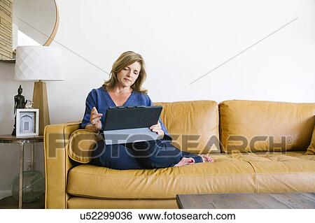Stock Photograph - Woman using digital tablet on sofa. Fotosearch