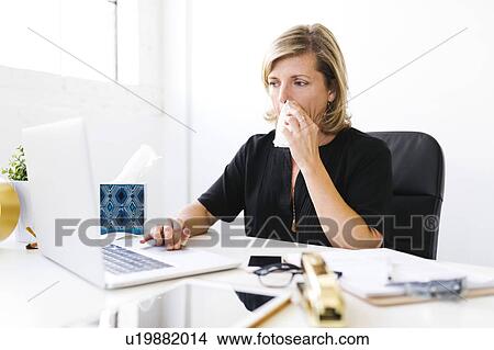 Woman using laptop, blowing nose View Large Photo Image Picture - Woman using laptop, blowing nose. Fotosearch