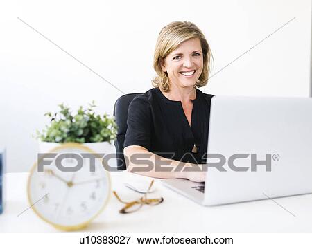Stock Photo - Woman using laptop, looking at camera. Fotosearch