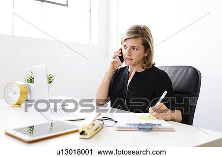Stock Image - Woman using mobile phone, looking at laptop. Fotosearch