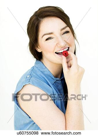 Stock Photo - Woman wearing blue top eating raspberry. Fotosearch