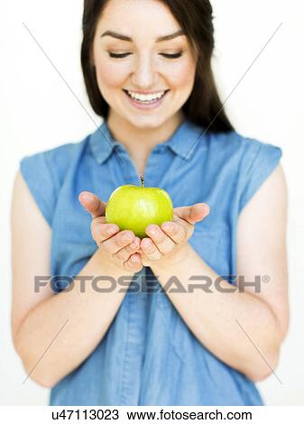 Stock Image - Woman wearing blue top holding green apple. Fotosearch