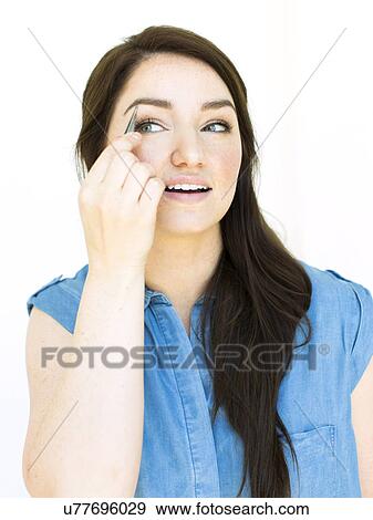 Stock Photo - Woman wearing blue top tweezing eyebrow. Fotosearch