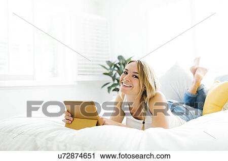 Stock Image - Woman with digital tablet lying on bed. Fotosearch