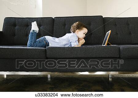Picture - Young boy (4-5) lying on sofa. Fotosearch