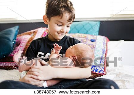 Stock Photo - Young boy (6-7) holding brother (2-5 months). Fotosearch