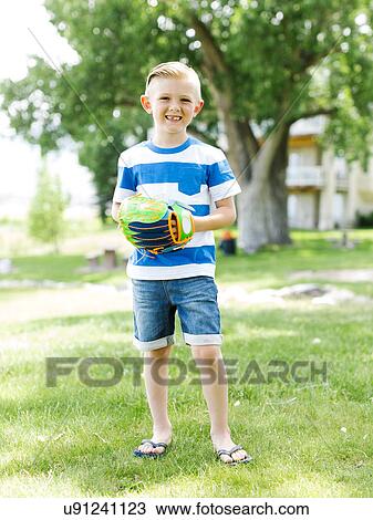 Stock Image - Young boy (6-7) with baseball glove standing in park. Fotosearch