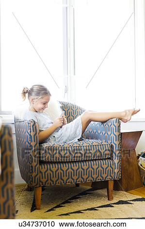 Stock Image - Young girl (6-7) sitting on armchair and using mobile phone. Fotosearch