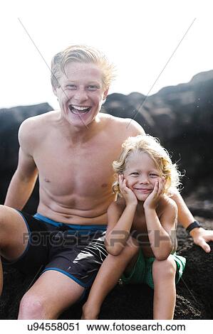 Stock Image - Young man with younger brother (4-5) sitting on rocks. Fotosearch
