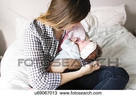Stock Image - Young mother with baby girl (0-1 months) sitting in bedroom. Fotosearch