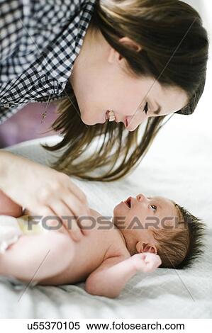 Stock Photography - Young mother with baby girl (0-1 months) lying on bed. Fotosearch