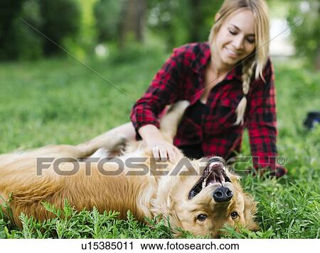 Stock Image - Young woman playing with golden retriever in park. Fotosearch