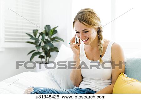 Young woman sitting on sofa and using smart phone View Large Photo Image Stock Photograph - Young woman sitting on sofa and using smart phone. Fotosearch