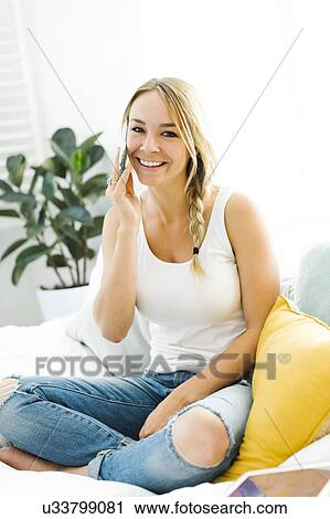 Stock Image - Young woman with mobile phone sitting on sofa. Fotosearch