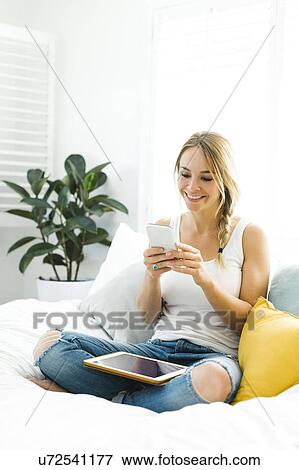 Young woman with mobile phone sitting on sofa View Large Photo Image Stock Photo - Young woman with mobile phone sitting on sofa. Fotosearch