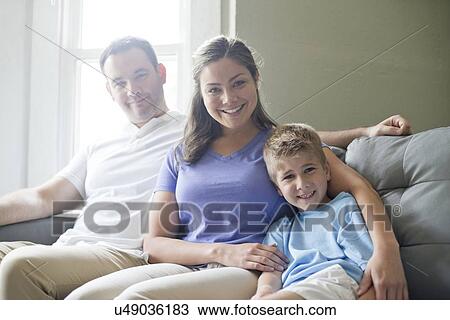 Stock Image - Boy sitting on sofa with his mother and father, portrait.. Fotosearch