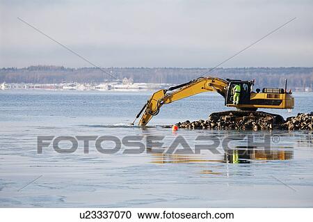 Stock Image - Bulldozer excavating rocks from the sea.. Fotosearch