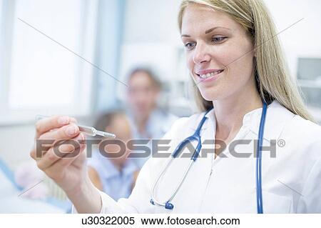 Stock Photography - Doctor looking at thermometer and smiling.. Fotosearch