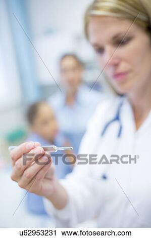 Stock Image - Doctor looking at thermometer.. Fotosearch