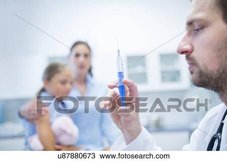 Stock Image - Doctor preparing injection, young girl in background.. Fotosearch