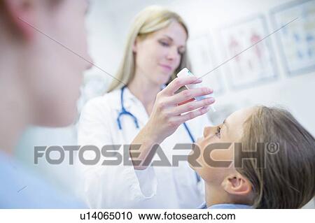 Stock Image - Doctor putting eye drops into young girl's eye.. Fotosearch