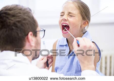 Stock Image - Doctor taking a swab from a young girl's mouth.. Fotosearch