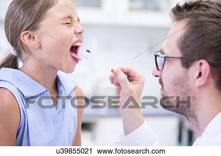 Stock Image - Doctor taking a swab from a young girl's mouth.. Fotosearch