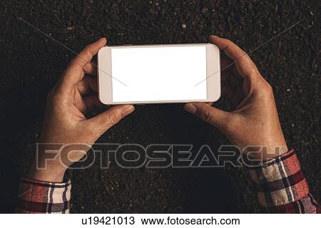 Stock Image - Farmer holding smartphone over soil. Fotosearch