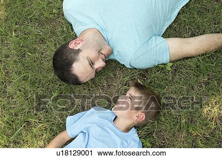 Stock Image - Father and son lying on grass, high angle.. Fotosearch