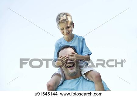 Picture - Father carrying son on shoulders, boy covering his father's e1 with hands.. Fotosearch