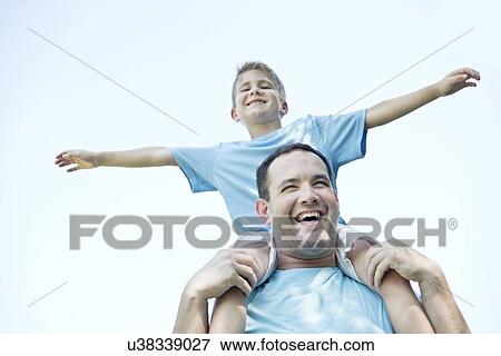 Stock Photo - Father carrying son on shoulders, boy with his arms out.. Fotosearch