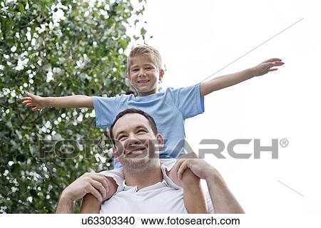 Stock Image - Father carrying son on shoulders with arms out.. Fotosearch