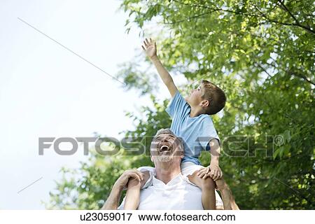 Grandfather carrying grandson on shoulders, boy reaching up to tree. View Large Photo Image Stock Photo - Grandfather carrying grandson on shoulders, boy reaching up to tree.. Fotosearch
