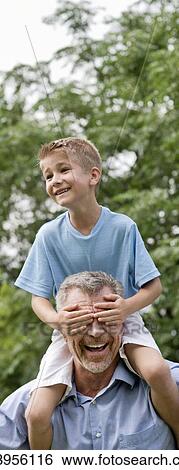 Grandfather carrying grandson on shoulders, boy covering grandfather's e1 with his hands. View Large Photo Image Stock Photograph - Grandfather carrying grandson on shoulders, boy covering grandfather's e1 with his hands.. Fotosearch