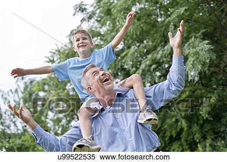 Stock Photography - Grandfather carrying grandson on shoulders with arms out.. Fotosearch