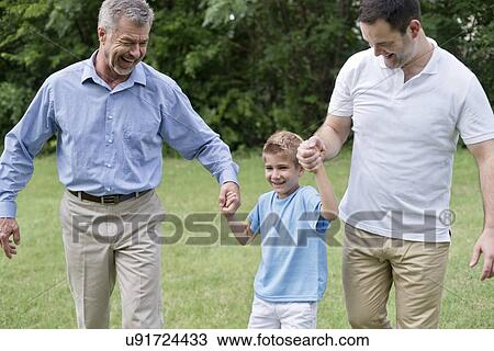 Stock Image - Grandfather, father and boy holding hands and smiling.. Fotosearch