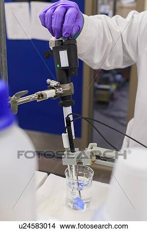 Picture - Lab technician adding reagent to sample while measuring pH.. Fotosearch
