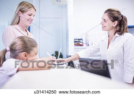 Medical receptionist smiling towards woman filling out paperwork, View Large Photo Image Stock Image - Medical receptionist smiling towards woman filling out paperwork,. Fotosearch