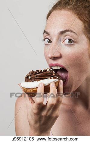 Stock Photography - MODEL RELEASED. Close-up of woman eating chocolate doughnut.. Fotosearch