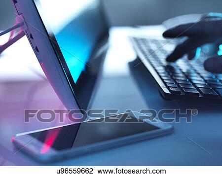 Stock Image - MODEL RELEASED. Computer use. Man working at PC with a mobile phone on the desk.. Fotosearch