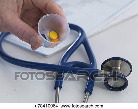 MODEL RELEASED. Doctor holding a cup containing prescription drugs ready to hand out to his patient. View Large Photo Image Picture - MODEL RELEASED. Doctor holding a cup containing prescription drugs ready to hand out to his patient.. Fotosearch