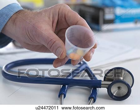 Stock Image - MODEL RELEASED. Doctor holding a cup containing prescription drugs ready to hand out to his patient.. Fotosearch