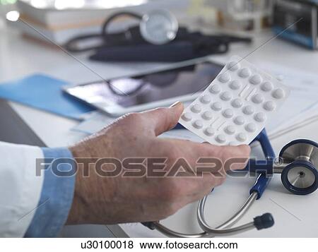 Stock Photo - MODEL RELEASED. Doctor holding a strip of drugs ready to hand out to his patient.. Fotosearch