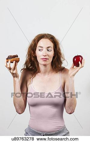 MODEL RELEASED. Indecisive woman holding apple and doughnut. View Large Photo Image Stock Photo - MODEL RELEASED. Indecisive woman holding apple and doughnut.. Fotosearch