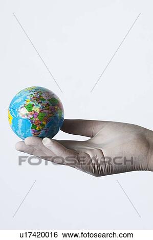 Stock Photograph - MODEL RELEASED. Person wearing latex glove holding small globe.. Fotosearch